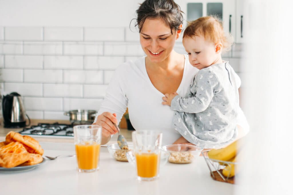 Mamá con bebé de 1 año desayunando fruta, leche y cereales